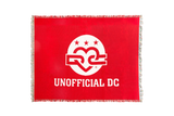 DC Red Tapestry Blanket — Jacquard woven cotton throw with a red field, the white Unofficial DC logo and three stars at the center, UNOFFICIAL DC lettering below, finished with fringe